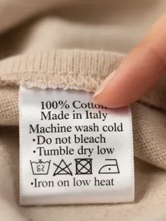 Hand pointing at a detailed clothing label with fabric and care symbols.