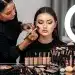 Professional makeup artist applying foundation to a model's face, surrounded by premium beauty products.