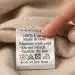 Hand pointing at a detailed clothing label with fabric and care symbols.
